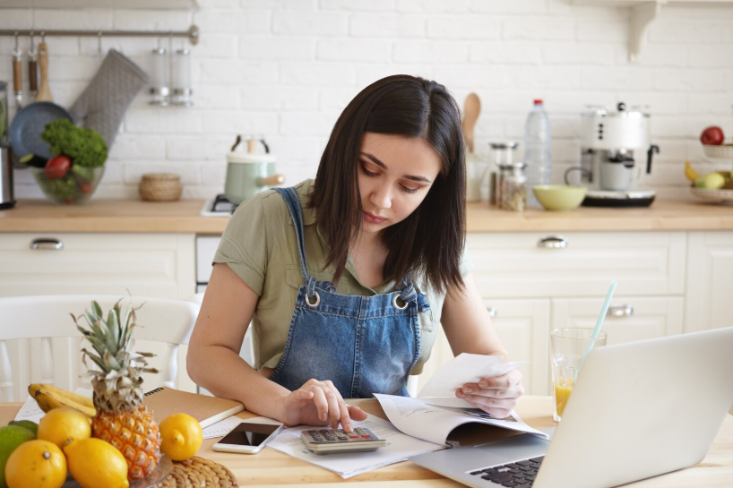 Woman reviewing receipts and expenses at the kitchen table to create an empowering budget.