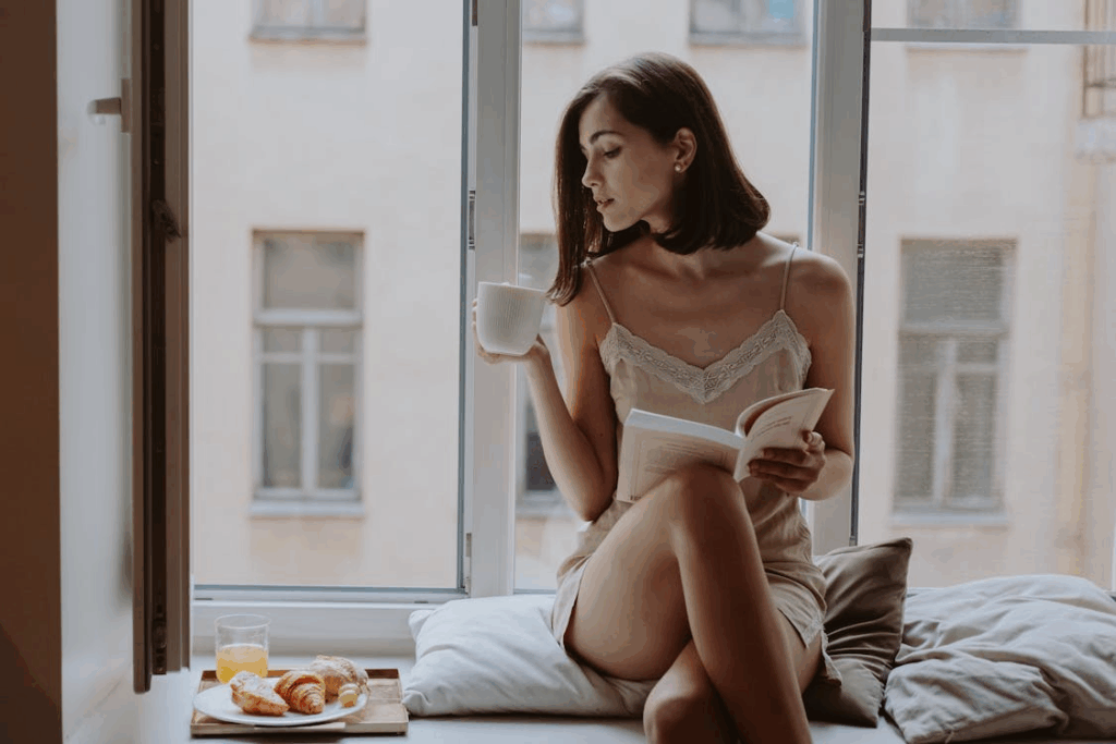 Woman enjoying daily ritual ideas on a budget while reading by the window with coffee.