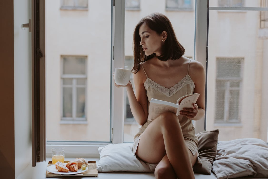 Woman enjoying daily ritual ideas on a budget while reading by the window with coffee.