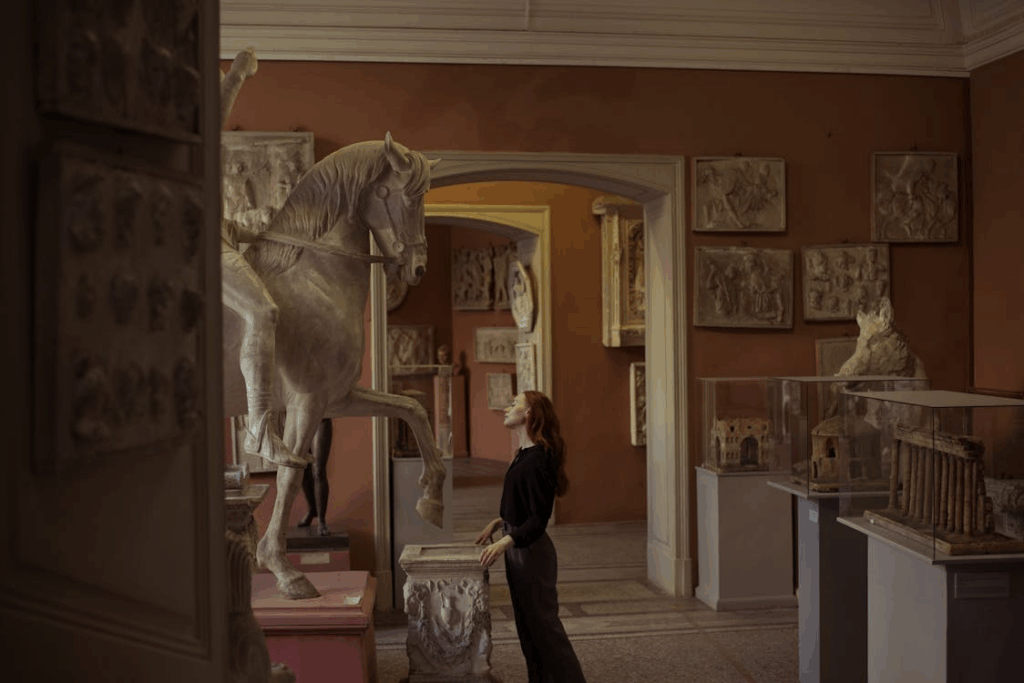 Woman observing a large horse sculpture inside a museum gallery filled with classical art.