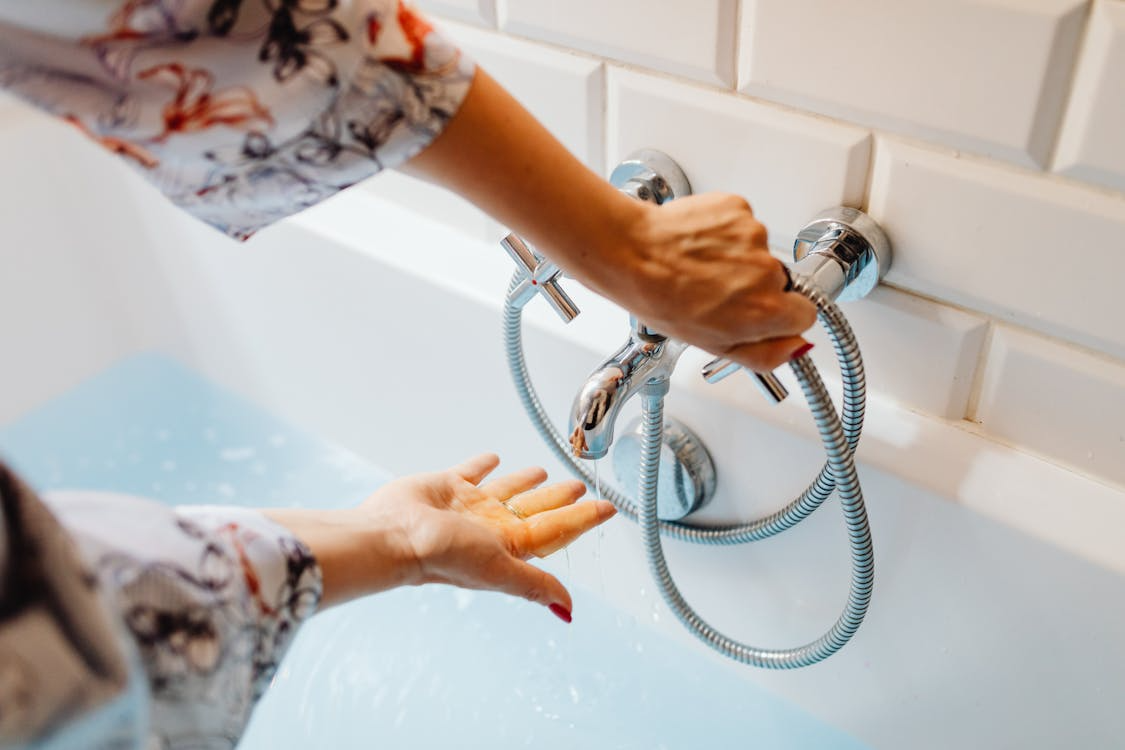 Person checking bathtub faucet temperature to identify hot water efficiency issues.